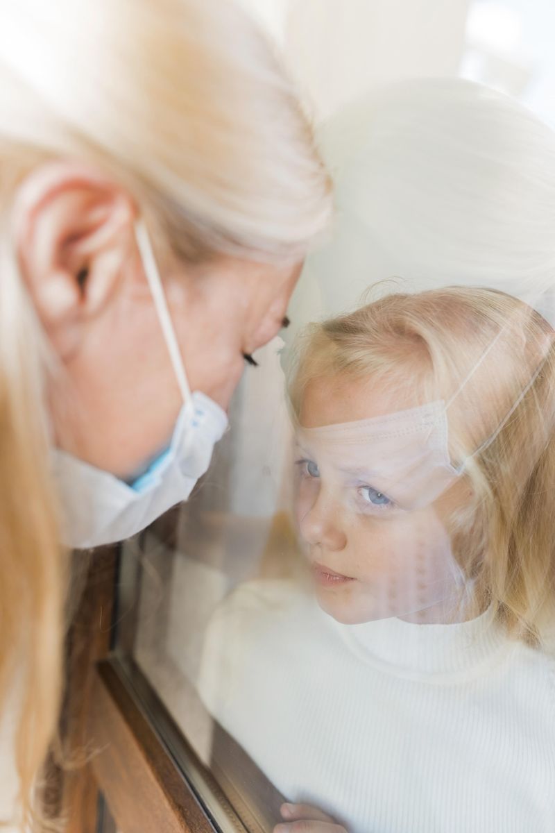 woman-with-medical-mask-quarantine-window-with-little-girl